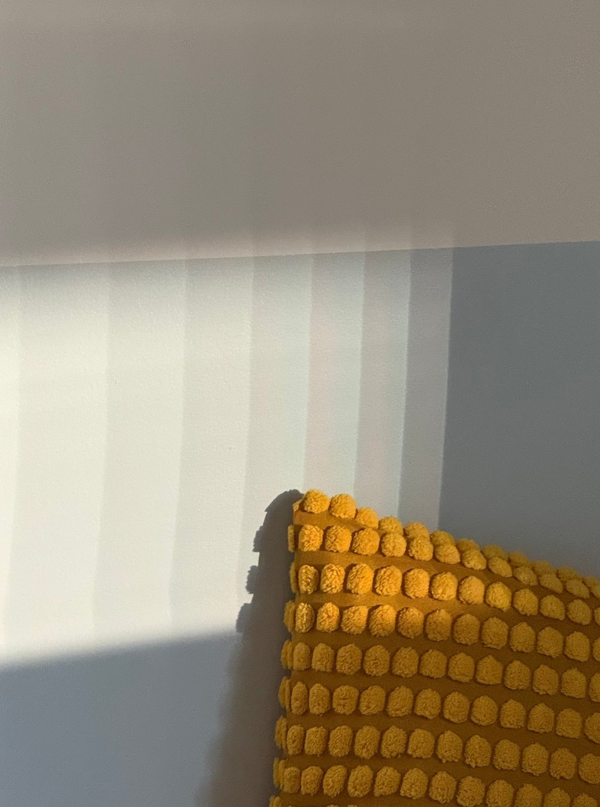 Yellow textured pillow against a white wall with reeded glass texture refracting onto the wall