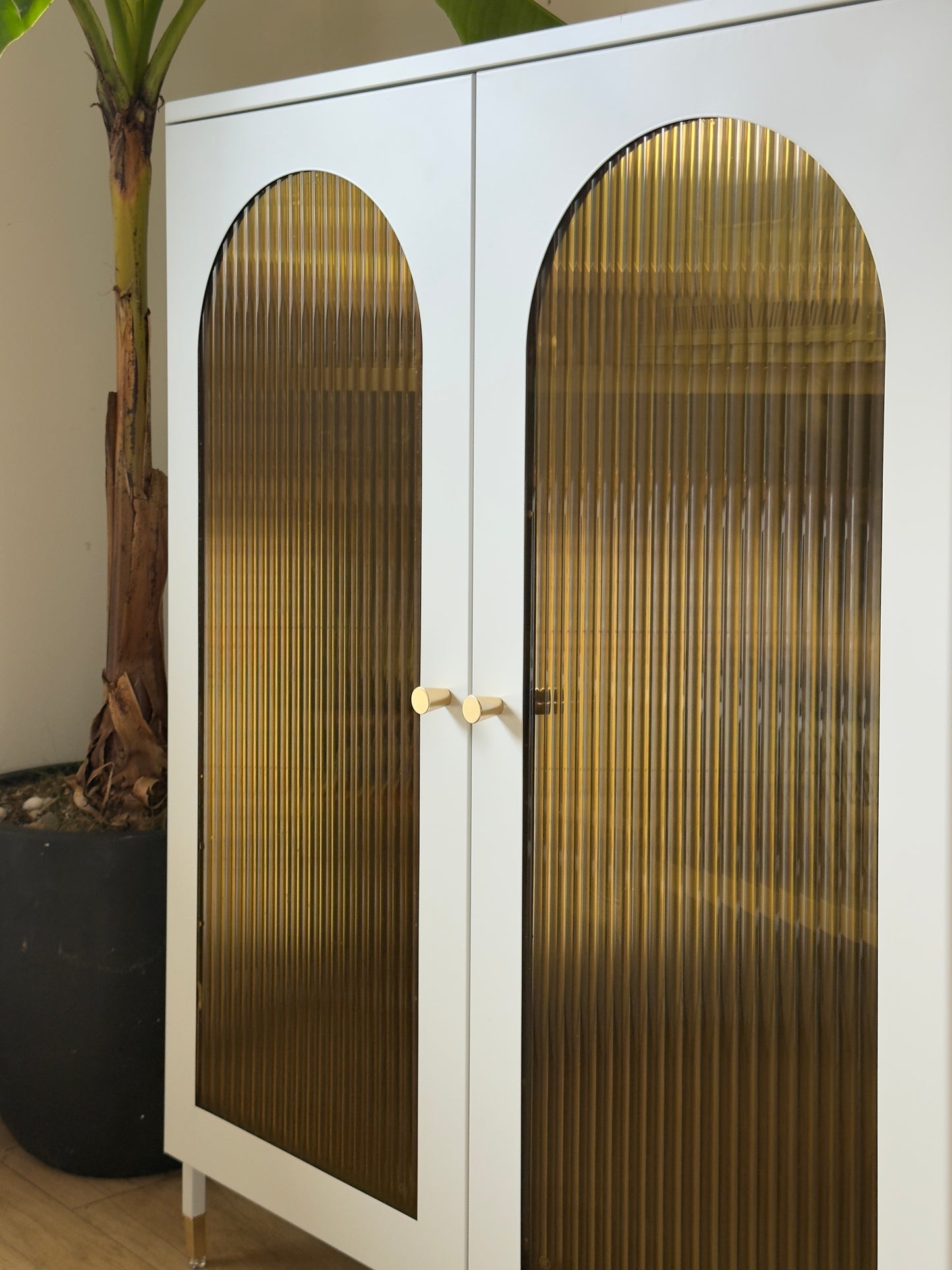 White cabinet with Amber coloured Reeded Glass window film on arched glass doors in a room setting.