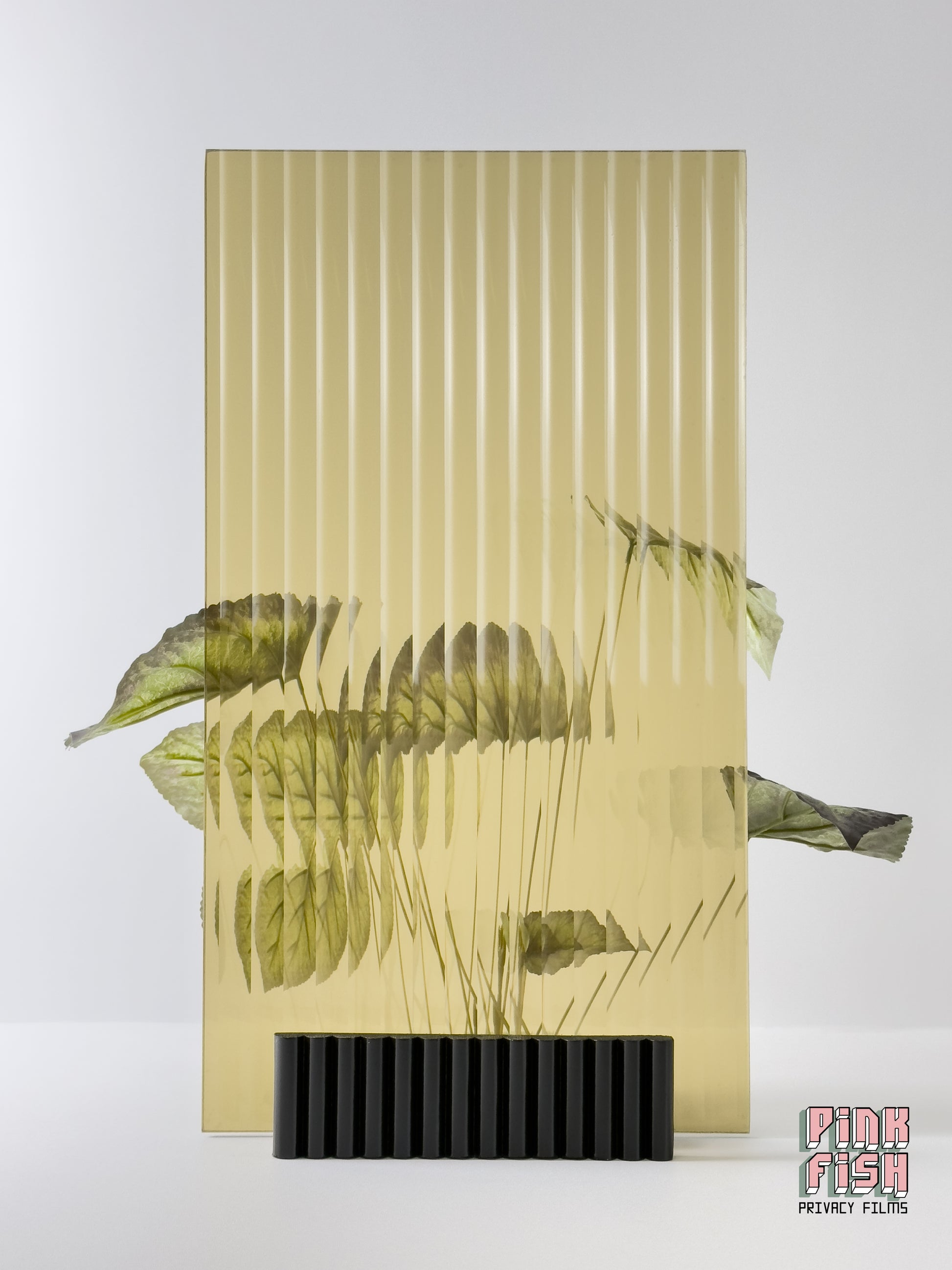 Amber Reeded Privacy Film on glass partition sitting in front of plant with 'Pink Fish Privacy Film' branding.