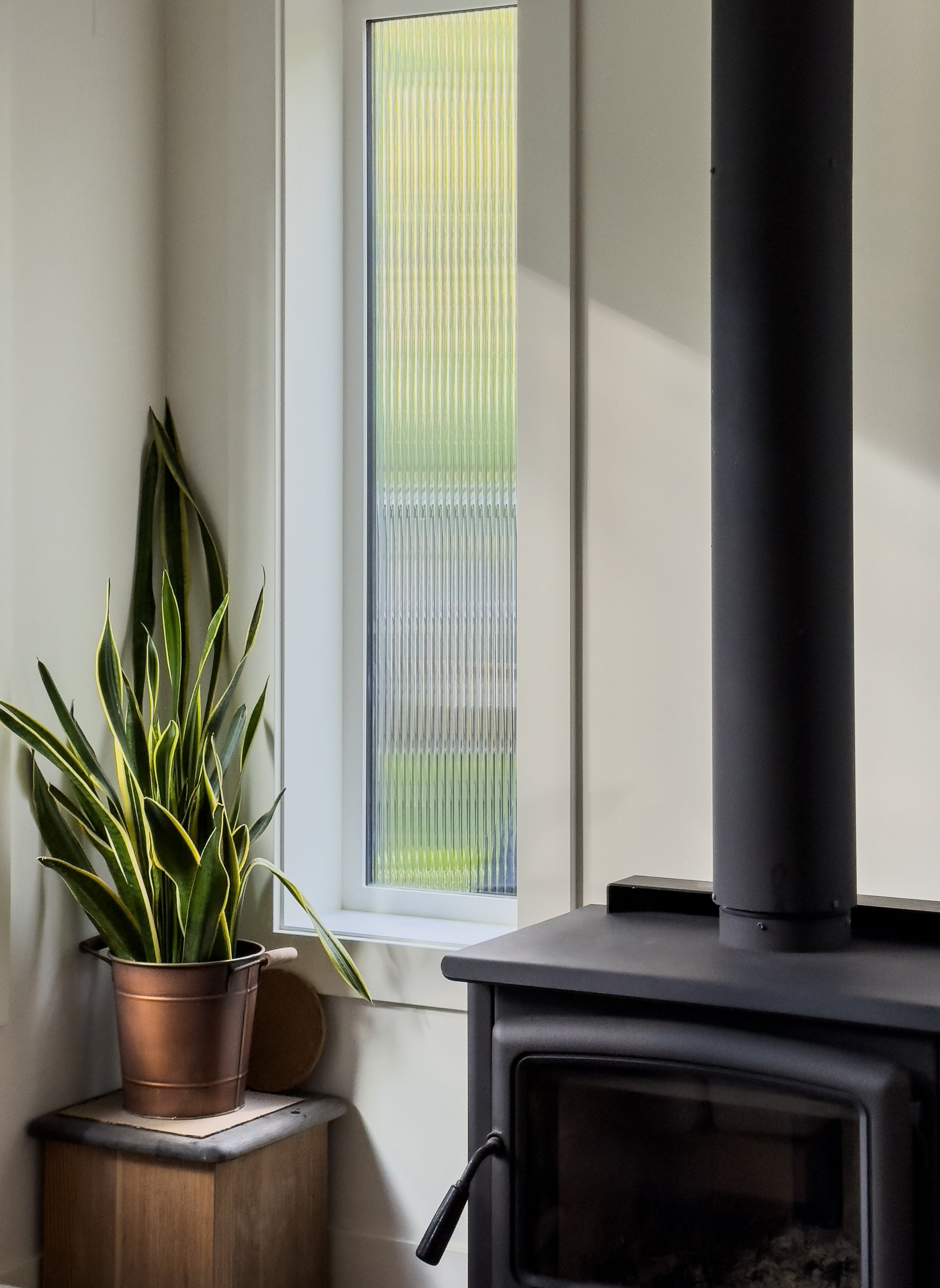 Black wood stove with a potted plant next to a window with Reeded Glass Window Film slightly blocking the views to outside.