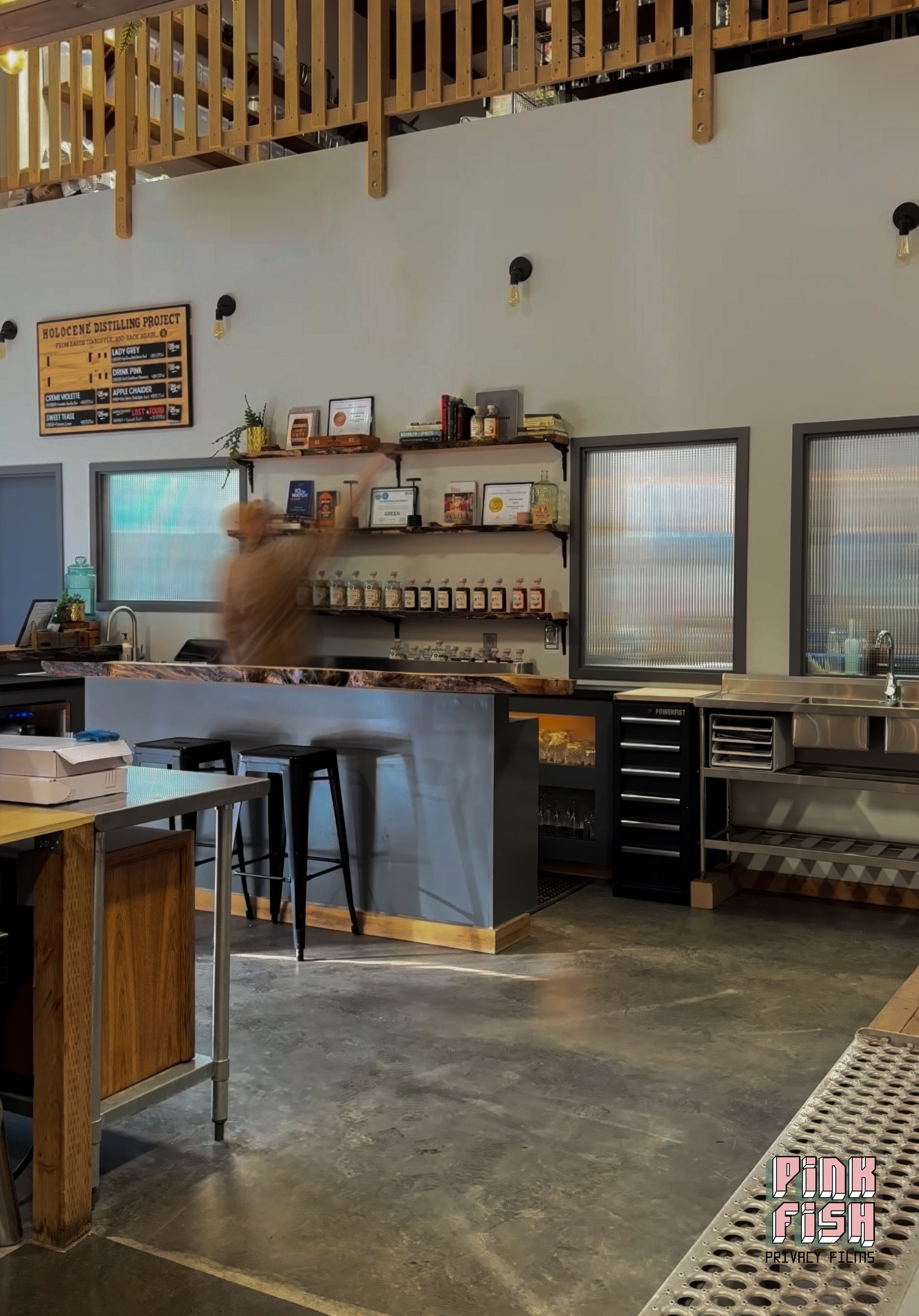 Modern interior of a liquor distillery with wooden furniture and large reeded glass window film on windows.
