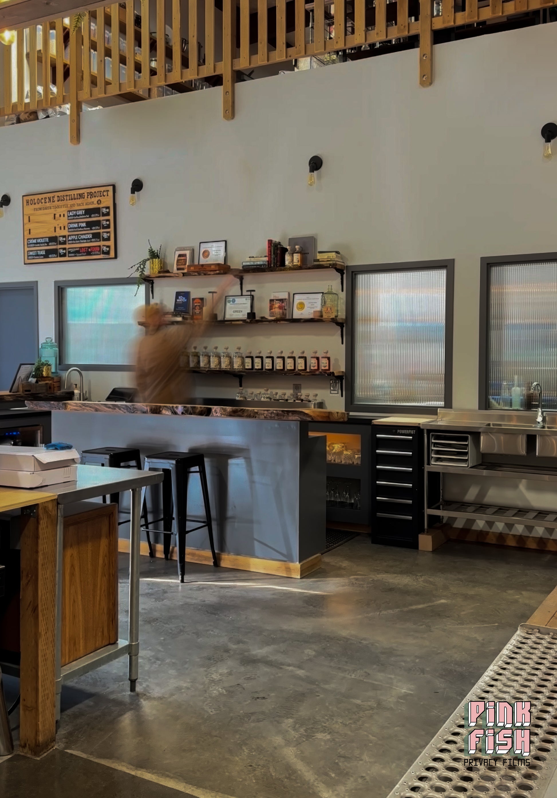 Modern interior of a liquor distillery with wooden furniture and large reeded glass window film on windows.